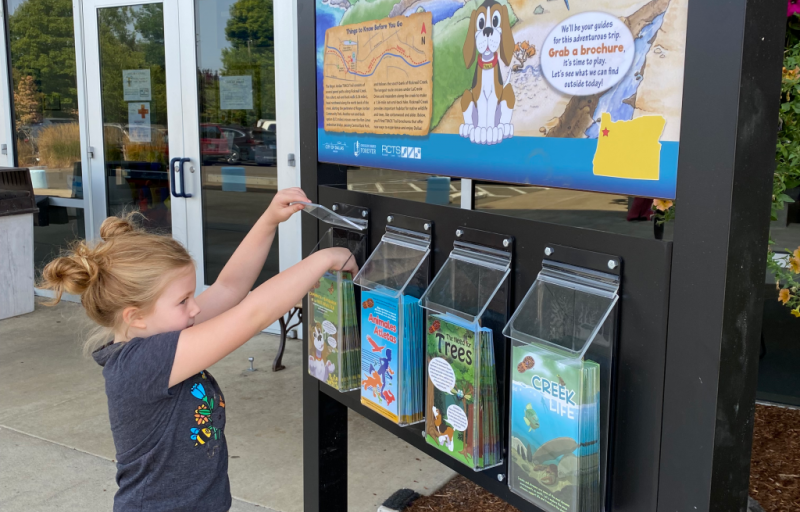 A child is reaching into the brochure holder on the TRACK Trail kiosk
