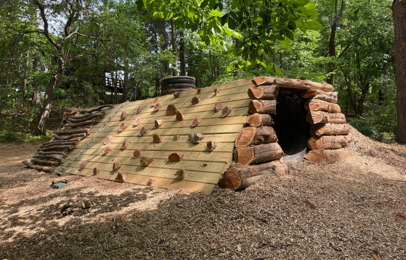 The nature playspace tunnel at Prairie Ridge Ecostation. A wooden tunnel made of planks and longs with climbing ropes and holds on the side.