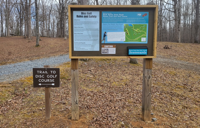 The trailhead sign for the disc golf course on a wooden kiosk.