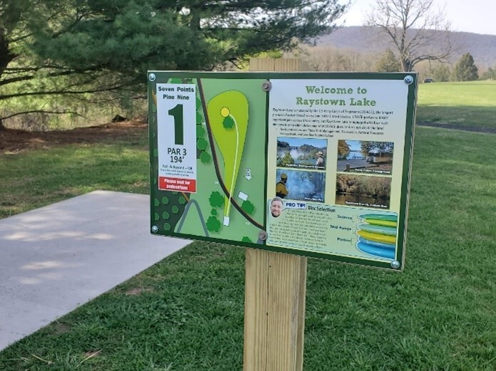 A tee sign at a disc golf course provides educational information.